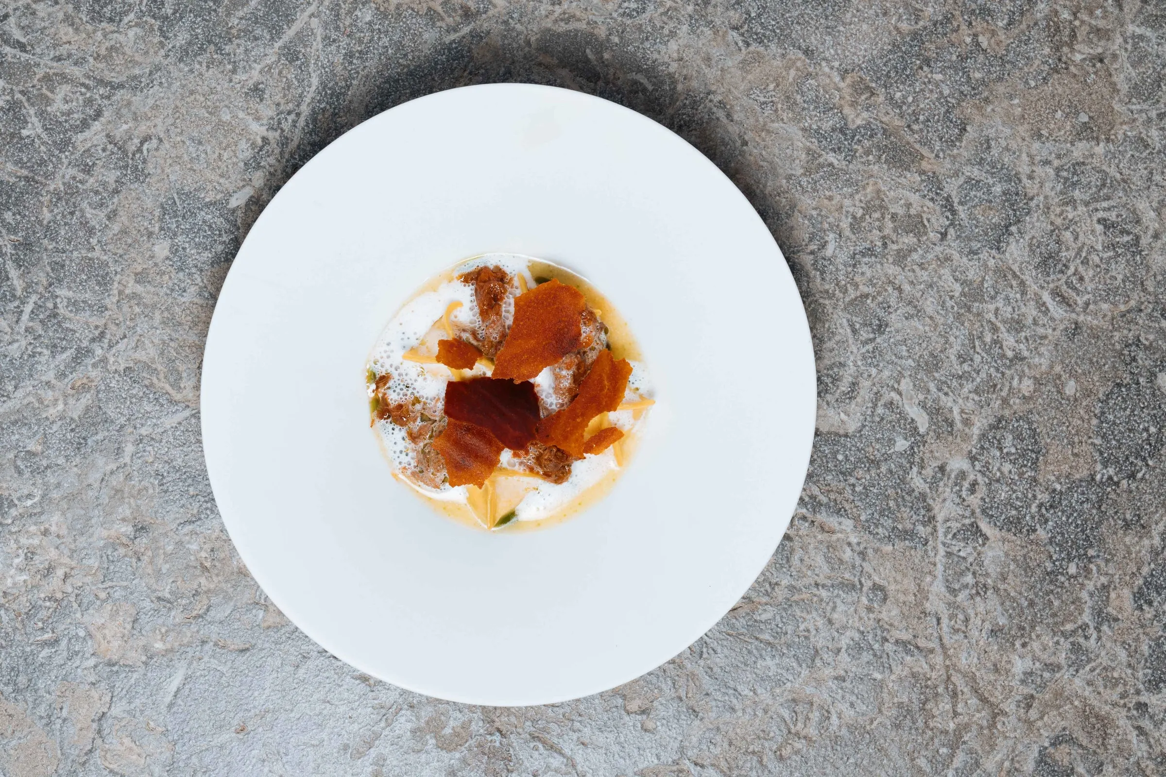 Een diep bord ravioli met ragù van Tajiri en schuim, op een stenen tafel